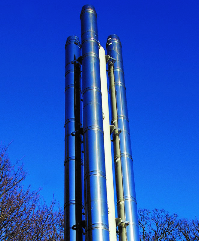 Three tall stainless steel industrial flues against a clear blue sky.