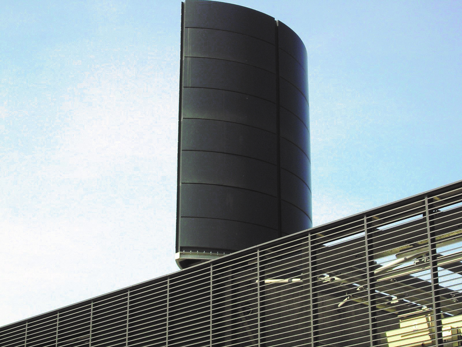 Close-up of a large cylindrical industrial stack on top of a modern building.